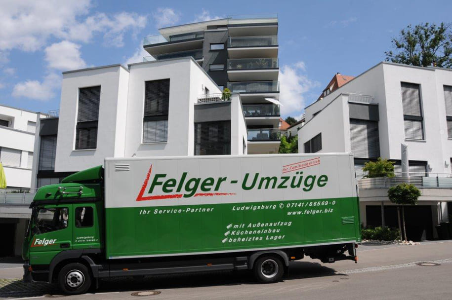 Grüner Umzugs-LKW von Felger-Umzüge auf der Straße vor modernen Mehrfamilienhäusern